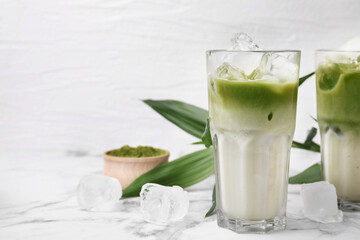 Glasses of tasty iced matcha latte and leaves on white marble table. Space for text