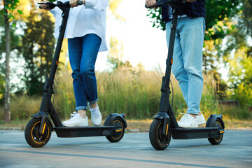 Couple riding modern electric kick scooters in park, closeup