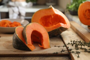 Cut fresh ripe pumpkin with aromatic thyme on wooden table in kitchen
