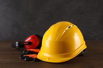 Hard hat, earmuffs and gloves on wooden table. Safety equipment - obrazy, fototapety, plakaty