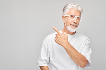 Gray-haired mature man 60 years old in white T-shirt pointing aside finger, demonstrating empty...
