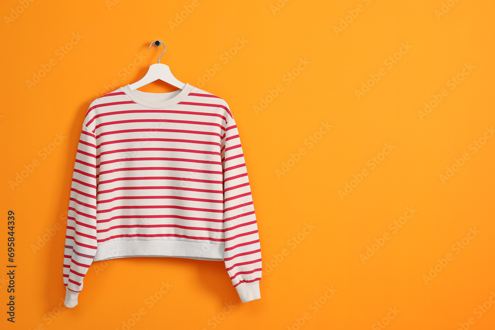 Wall mural Hanger with striped sweatshirt on orange wall, space for text