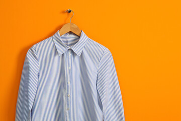 Hanger with striped shirt on orange wall, space for text