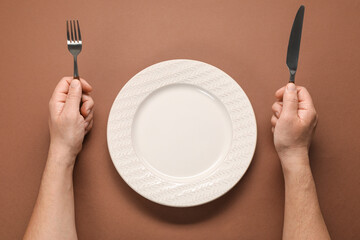 Man with cutlery and empty plate at brown table, top view