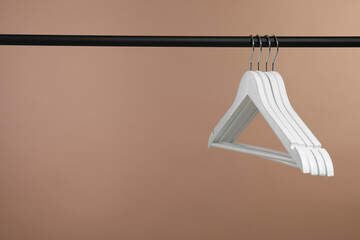 Empty clothes hangers on rack against light brown background. Space for text