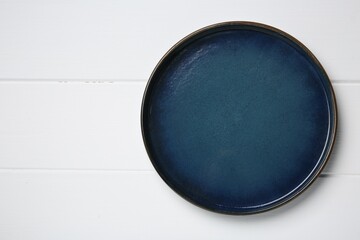 One dark blue ceramic plate on white wooden table, top view. Space for text