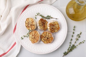 Heads of fried garlic with thyme and oil on white table, flat lay