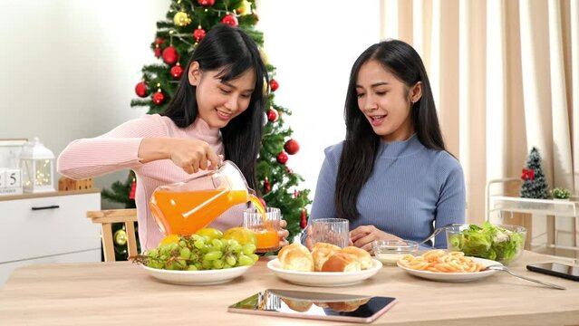 Happy two asian female friends to happiness having drinks and eating by talking of Christmas holiday celebration at home