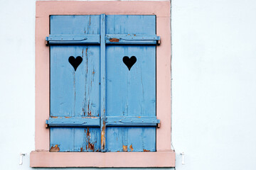 The closed window shutter is blue with cracked paint and a symmetrical pattern