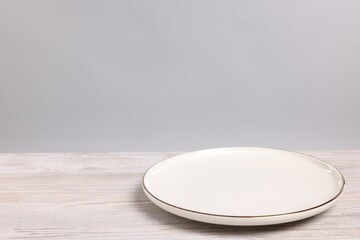 Empty ceramic plate on wooden table against light background, space for text