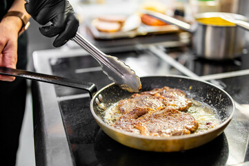 Professional chef cooking beef steak in frying pan on stove in restaurant kitchen