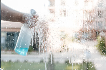 a man's hand with a window cleaning spray applies foam to the window. - obrazy, fototapety, plakaty