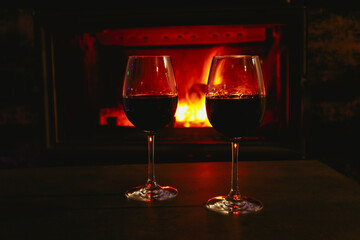 Two glasses of red wine on a background of a burning fireplace. Cozy atmosphere winter evening.