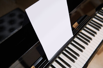Close-up old black wooden piano with ivory and ebony piano keys and white paper sheet with copy...