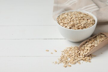 Bowl and scoop with oatmeal on white wooden table, space for text