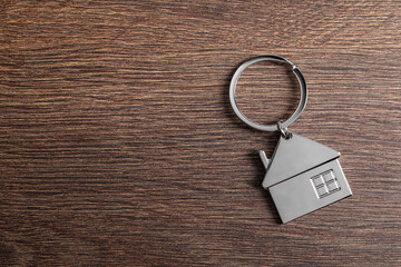 Metal keychain in shape of house on wooden table, top view. Space for text