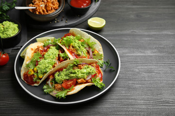 Delicious tacos with guacamole, meat and vegetables on wooden table, space for text