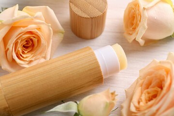 Lip balm and rose flowers on white wooden background, closeup