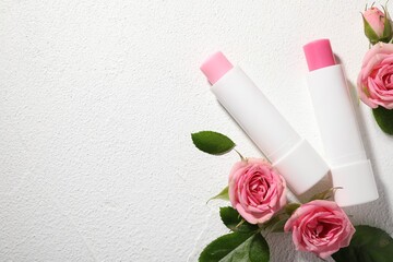 Lip balms and rose flowers on white textured background, flat lay. Space for text