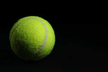 One tennis ball on black background, closeup. Space for text