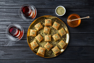 Delicious fresh baklava with chopped nuts served on black wooden table, flat lay. Eastern sweets