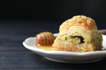 Delicious fresh baklava with chopped nuts and honey on black wooden table, closeup with space for text. Eastern sweets