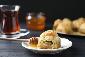 Delicious fresh baklava and honey with chopped nuts on black wooden table, closeup. Eastern sweets
