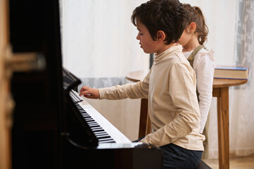 Handsome kids a teenage boy and little child girl, playing grand piano together during a music...