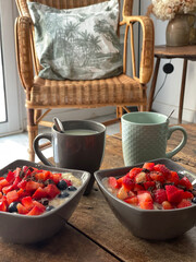 Plano inclinado de dos tazones de desayuno con fruta y dos tazas con bebida sobre una mesa de...