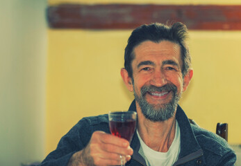 An elderly gentleman with a broad grin is raising a glass of alcoholic beverage in a toast.