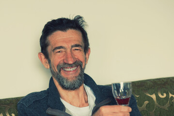 An elderly gentleman with a broad grin is raising a glass of alcoholic beverage in a toast.