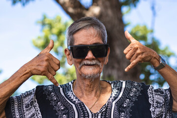 A cool hippie granddad making the shaka sign, gesturing with both his hands. Wearing shades and...