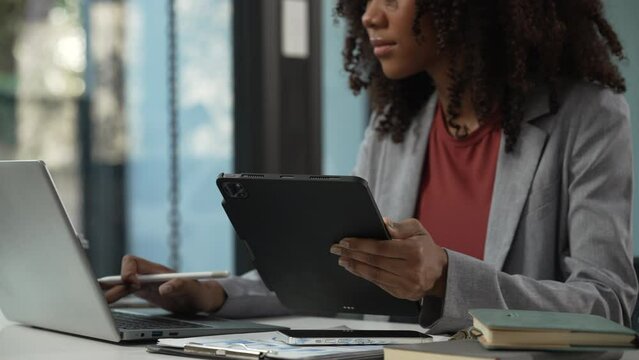 smiling African American university student with an afro hairstyle, holding a tablet and sitting at a desk with a laptop. online class learning from video conference