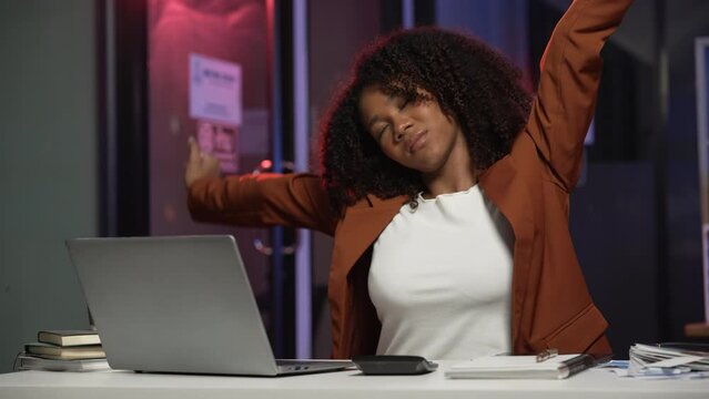 bored African American office worker with an afro, resting her cheek on her hand while looking at a laptop screen.	
