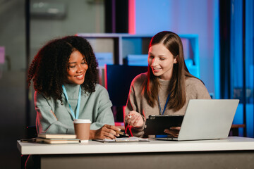 African American trainee with an afro and a Caucasian colleague working together in an office, possibly during overtime.