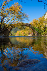 Beautiful view of An Ottoman bridge above the peaceful Voidomatis river, in a fantastic morning backlight, Klidonia Bridge, Greece.