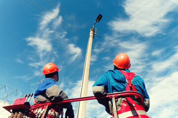 Two professional electricians look up at a street lamp on a summer day against the sky....