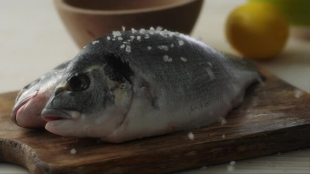 Raw Fish on a Wooden Board gets Sprinkled with Salt. Close-up, shallow dof.
