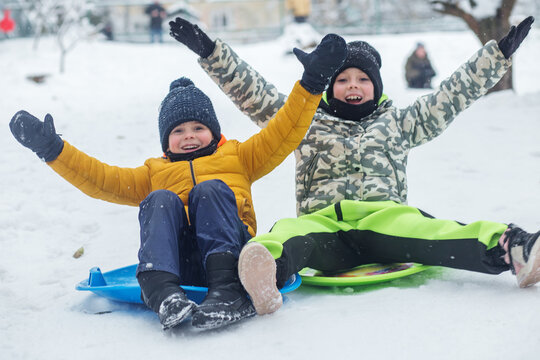 Children ride on snow plate and having fun. Outdoor play. Cold temperature. Winter time