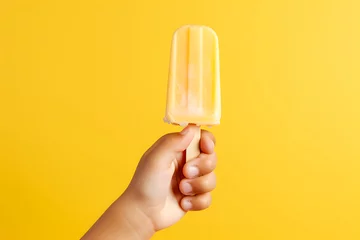 Foto op Aluminium Side view of a child's hand holding fruit ice cream isolated on a yellow background © Marina Shvedak
