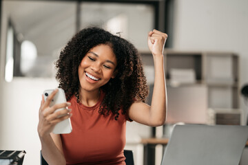 Happy black woman holding a smartphone, happy smiling, getting bonus money.