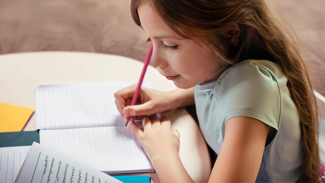 Uma menina de cabelos compridos, escrevendo em um caderno. Conceito de volta às aulas.