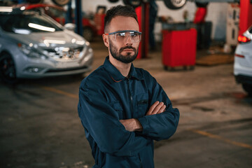 Standing and posing. Car repairman is in the garage with automobile