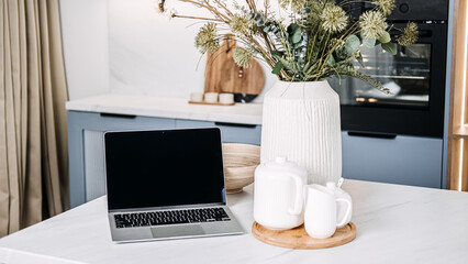Home Office Setup with Laptop and Cozy Kitchen Decor. A chic home office setup featuring an open laptop on a marble countertop, complemented by a warm kitchen ambiance and stylish decor.