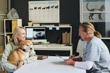 Veterinarian talking to joyful female dog owner during appointment in clinic