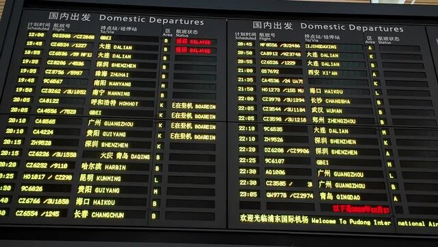 Domestic flight information board displaying departure times, destinations, flight numbers, and boarding statuses with delays at an airport terminal, Shanghai, China
