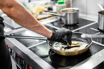 Professional chef cooking mushroom in frying pan on stove in restaurant kitchen