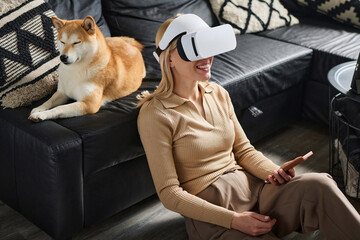 Young woman wearing vr headset sitting on floor indoors with her dog sleeping on couch
