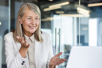 Senior female boss smiling talking remotely with colleagues partners, experienced gray-haired...