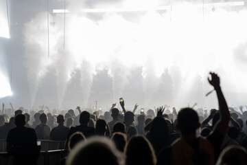 Crowd of people attending a performance. Bright light coming from the stage with smoke effects